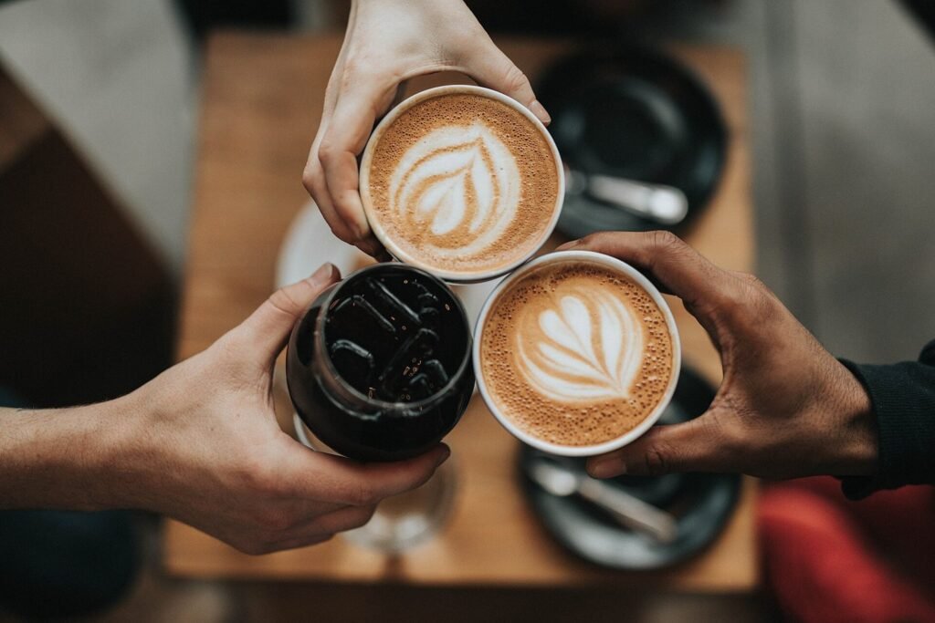 Three hands raising cups of coffee together above a wooden table.